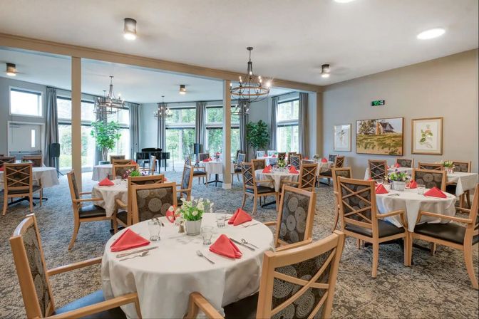 A restaurant with round tables set with red napkins and tall windows.