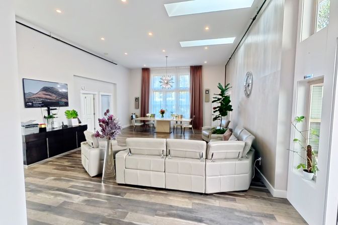 The living room, with a sectional sofa under skylights and a dining table by tall windows.